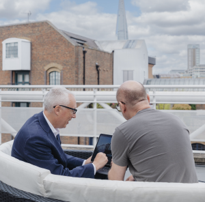 Two men look at a tablet on a rooftop in London